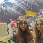 Dwie dziewczynki uśmiechają się do aparatu. W tle hala