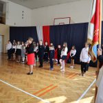 Grupa uczniów przed występem. Po prawej stronie poczet sztandarowy