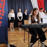 Dziewczynka w białej bluzce i czarnych spodniach gra na keyboardzie