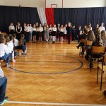 Uczniowie podczas występu. Po bokach zgromadzeni na widowni uczniowie i nauczyciele.