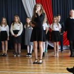 Dziewczyna w czarnej sukience śpiewa piosenkę.