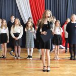 Dziewczyna śpiewa piosenkę, z tyłu zasłuchani uczniowie