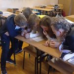 Pięcioro uczniów pochyla się nad kartką papieru – uczniowie rozwiązują quiz o patronie.