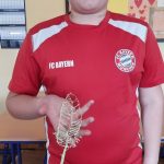 Chłopiec w czerwonym podkoszulku trzyma w ręku pracę wykonaną długopisem 3d (ptasie pióro).