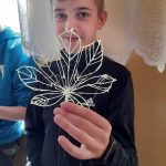 chłopiec ubrany w czarny dres, trzyma w ręku liść wykonany długopisem 3d.