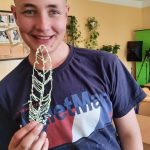 Chłopiec w granatowym podkoszulku stoi na tle klasy, trzyma w ręku pióro wykonane techniką 3d.