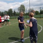 Pani dyrektor wręcza dyplom chłopcu w czarnej koszulce i spodenkach , w tle dzieci ustawieni w czterech rzędach.