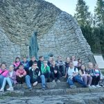 Grupa dzieci siedzi obok figury Matki Bożej w Pasierbcu