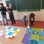 Dwóch chłopców stoi przed matą i programują pracę Photona, a dwóch głaszcze swojego Photona, by ruszył dalej.