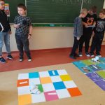 Dwaj chłopcy rozwiązują zadanie wybrane przez Photona. Grupa trzyosobowa stoi przed matą i programuje Photona