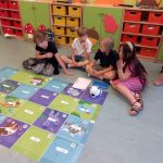 Czwórka dzieci siedzi na podłodze obok kolorowej maty, na której znajduje się robot.