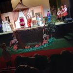 Scena, na niej grupa osób, w środku klęczy młoda para, przed nią stoi królowa i dworzanin