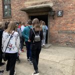 Uczniowie odwróceni tyłem do aparatu wchodzą do baraku nr 6