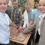 Kilkoro uśmiechniętych uczniów stoi nad tablicą wyklejoną zdjęciami głów różnych ludzi