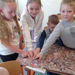 Chłopiec w szarej bluzie i dwie dziewczynki w jasnych koszulkach wskazują miejsce, w którym wypatrzyli zdjęcie twarzy Stanisława Miłkowskiego