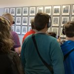 Uczniowie odwróceni tyłem oglądają zdjęcia pierwszych więźniów obozu