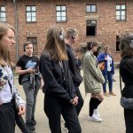 Grupa uczniów przy jednym z baraków obozowych