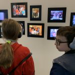 Chłopiec i dziewczynka stoją przy ścianie oglądając zdjęcia osób, którym udało się przeżyć obóz