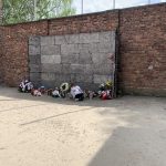 Ściana śmierci, przed nią dziewczynka zapalająca znicz