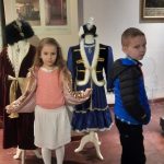 Dzieci pozują na tle ekspozycji strojów szlacheckich.