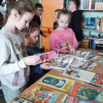 Dzieci przeglądają książki ułożone na stolikach.