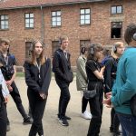 grupa uczniów ubranych w ciemne ubrania stoi obok budynku z czerwonej cegły