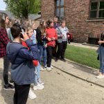 Uczniowie stoją na chodniku, słuchają opowiadania pani przewodnik