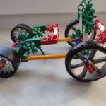 pojazd czterokołowy zbudowany z klocków lego. Czarne koła, zielono czerwone elementy nadwozia.