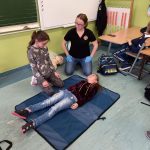 Dziewczynka i kobieta klęczą przed leżącą na podłodze dziewczynką.