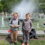 Dwaj chłopcy stoją przed tryskającą wodą fontanną