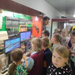 Uczniowie oglądają gry komputerowe w muzeum, jeden z nich trzyma w ręce pad do gry