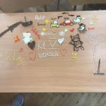 Na ławce leżą kolorowe rysunki i napisy uczniów.