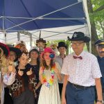 dziesięć osób, które są poprzebierane w stroje wykorzystywane w fotobudce – kapelusze, wąsy, peruki, maski.