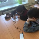 Dwie uczennice siedzące przy ławce, jedna trzyma długopis, druga podpiera ręka głowę.