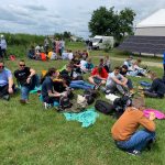 Duża grupa osób siedzi na trawie na karimatach