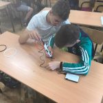 Dwóch uczniów siedzących przy ławce, jeden trzyma długopis, drugi przytrzymuje filament.