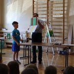 Mężczyzna pokazuje stojącemu chłopcu kartki: zieloną i białą. Na zielonej są dwa czerwone pasy, na białej jeden - żółty