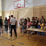 Mążczyzna stojący tyłem do aparatu rozdaje zgromadonym dzieciom dyplomy