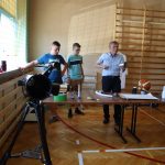 Nauczyciel trzyma w ręce puszkę, pokazując że jest pusta, obok niego stoją dwaj uczniowie