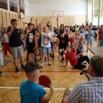 Duża grupa uczniów na sali gimnastycznej zgłasza się do wykonania zadania