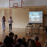 Chłopiec i dziewczynka stoją na środku sali, obok nich ekran z filmem z projektora