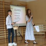 Dziewczyna w błękitnej sukience mówi do mikrofonu, obok niej stoi chłopiec. Za nimi ekran z napisem szlafrok